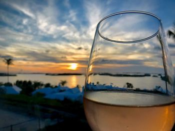 Close-up of glass of water against sky during sunset