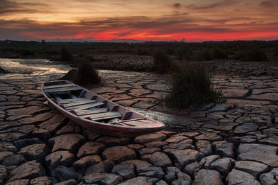 Boat on drought land against sky during sunset