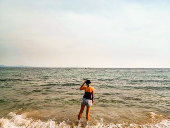 Rear view of man standing on beach against sky