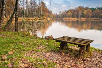 Park bench by lake against sky during autumn