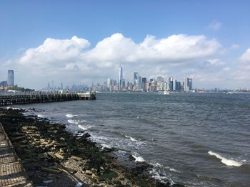 Sea by modern buildings against sky in city