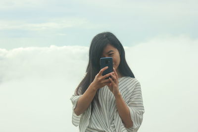 Smiling young woman taking selfie against sky