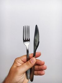 Cropped hand of man holding silverware against white background