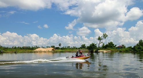 Men riding boat in lake against cloudy sky