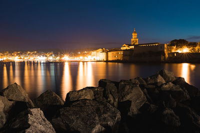 Illuminated buildings by river against sky at night