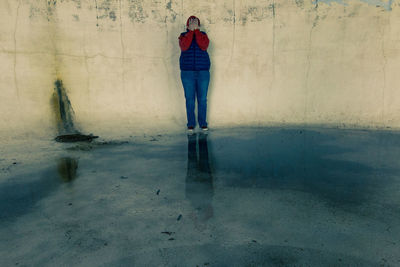 Full length of woman covering face while standing against wall