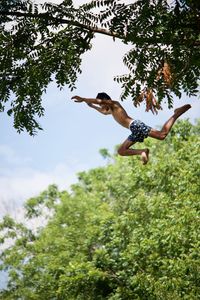 Low angle view of boy jumping tree against sky