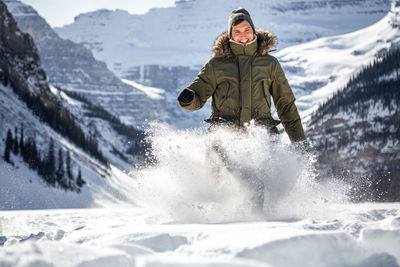 Portrait of man playing with snow on land against mountain