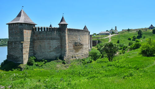 Khotyn fortress by grassy field against clear blue sky