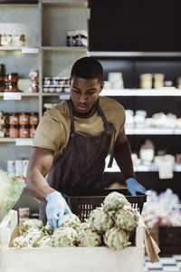 Male entrepreneur arranging food product in basket at delicatessen shop