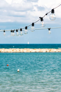 Vintage hanging light bulbs with blue sky, white clouds, blue sea, sail boat and breakwater