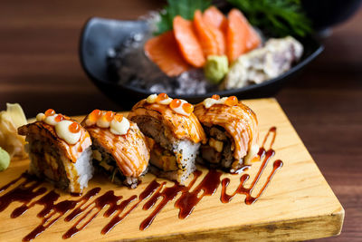 Grilled sushi nigiri rolls on wooden plate with blurred fresh salmon sashimi. japanese food