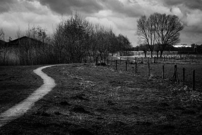 Bare trees on field against cloudy sky