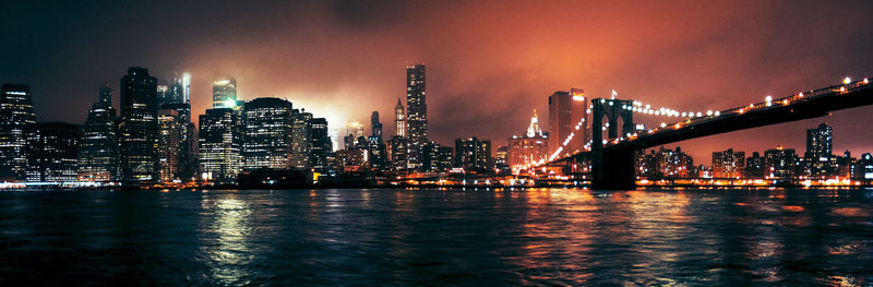 Illuminated city by river against sky at night