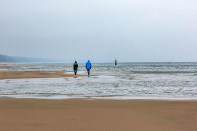 Rear view of people walking at beach against sky