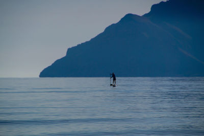 Man paddleboarding in sea against mountain