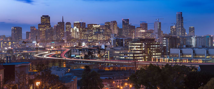 Illuminated city by buildings against sky at dusk