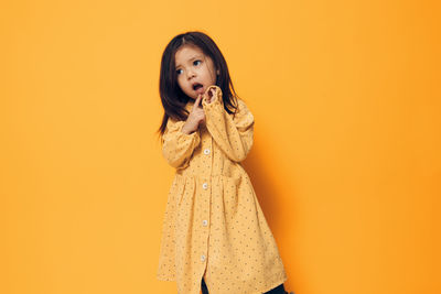 Young woman standing against yellow background