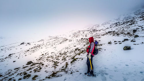 Side view of woman standing on snowcapped mountain against clear sky