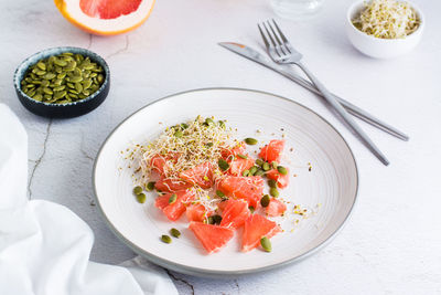 Fresh salad of grapefruit, clover and alfalfa sprouts and pumpkin seeds and cutlery on a plate 