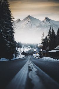 Snow covered road by trees against sky