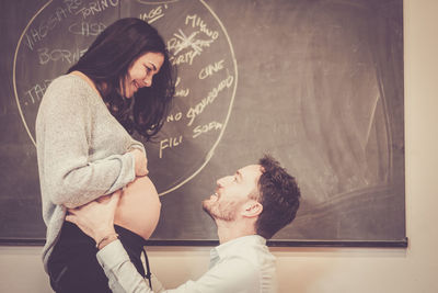 Side view of pregnant woman looking at man against blackboard