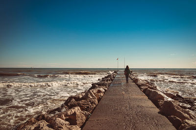 Rear view of man standing on beach against clear sky