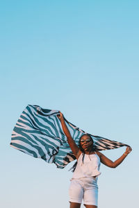 Low angle view of woman holding umbrella against clear blue sky