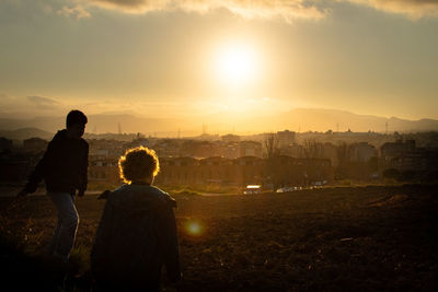 Boys looking at cityscape against sky during sunset