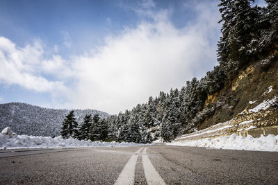 Road by trees against sky during winter