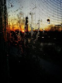 Silhouette fence against orange sky seen through glass window