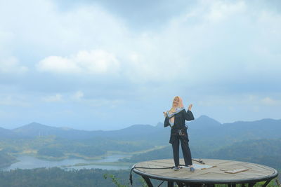 Portrait of smiling woman standing on built structure against mountains