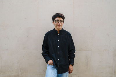 Young transgender man leaning on a wall while posing outdoors on the street.