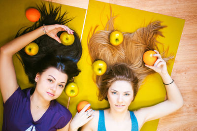 Portrait of smiling young friends with apples lying on hardwood floor