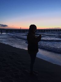 Silhouette woman standing on beach against sky during sunset