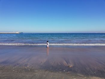 Boy standing on sea shore against clear sky