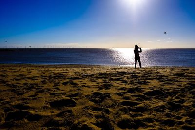 Silhouette boy standing on beach against sky during sunset