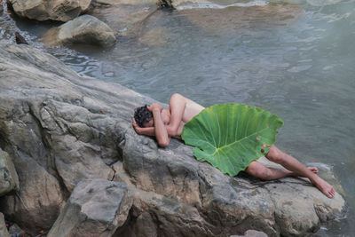 High angle view of man holding leaf while lying on rock
