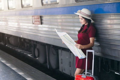 Woman reading map while standing against train at railroad station platform