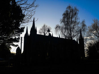 Low angle view of silhouette trees and building against sky