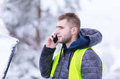 Young man talking over mobile phone while standing outdoors during winter