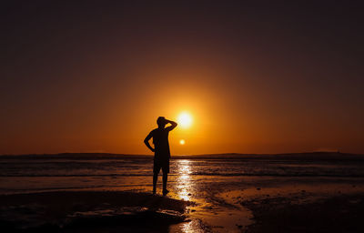 Silhouette man standing at beach against sky during sunset