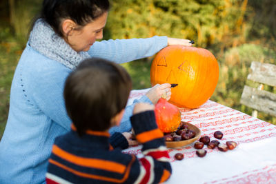 Woman with boy drawing on pumpkin in back yard for halloween