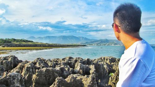 Portrait of man wearing sunglasses standing on rock against sky