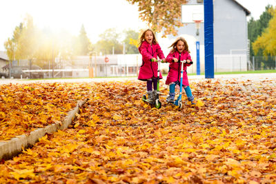 Girls riding push scooters at park during autumn