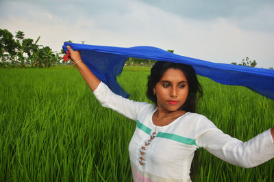 Portrait of young woman standing on field against sky