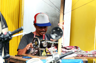 Mid adult man stitching fabrics while sitting in workshop