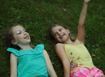 Close-up of smiling sisters wearing make-up while lying on field