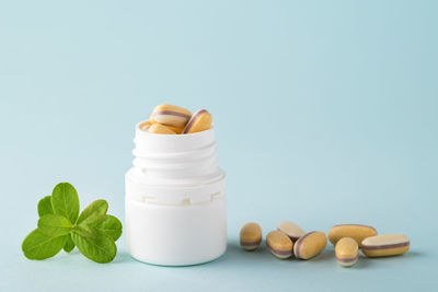 Vitamins and herbal supplements in jars with a green plant on a blue background. 