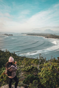 Rear view of woman photographing by trees and sea against sky